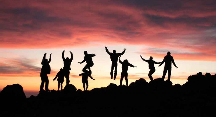 the silhouette of nine people jumping into the air at sunset